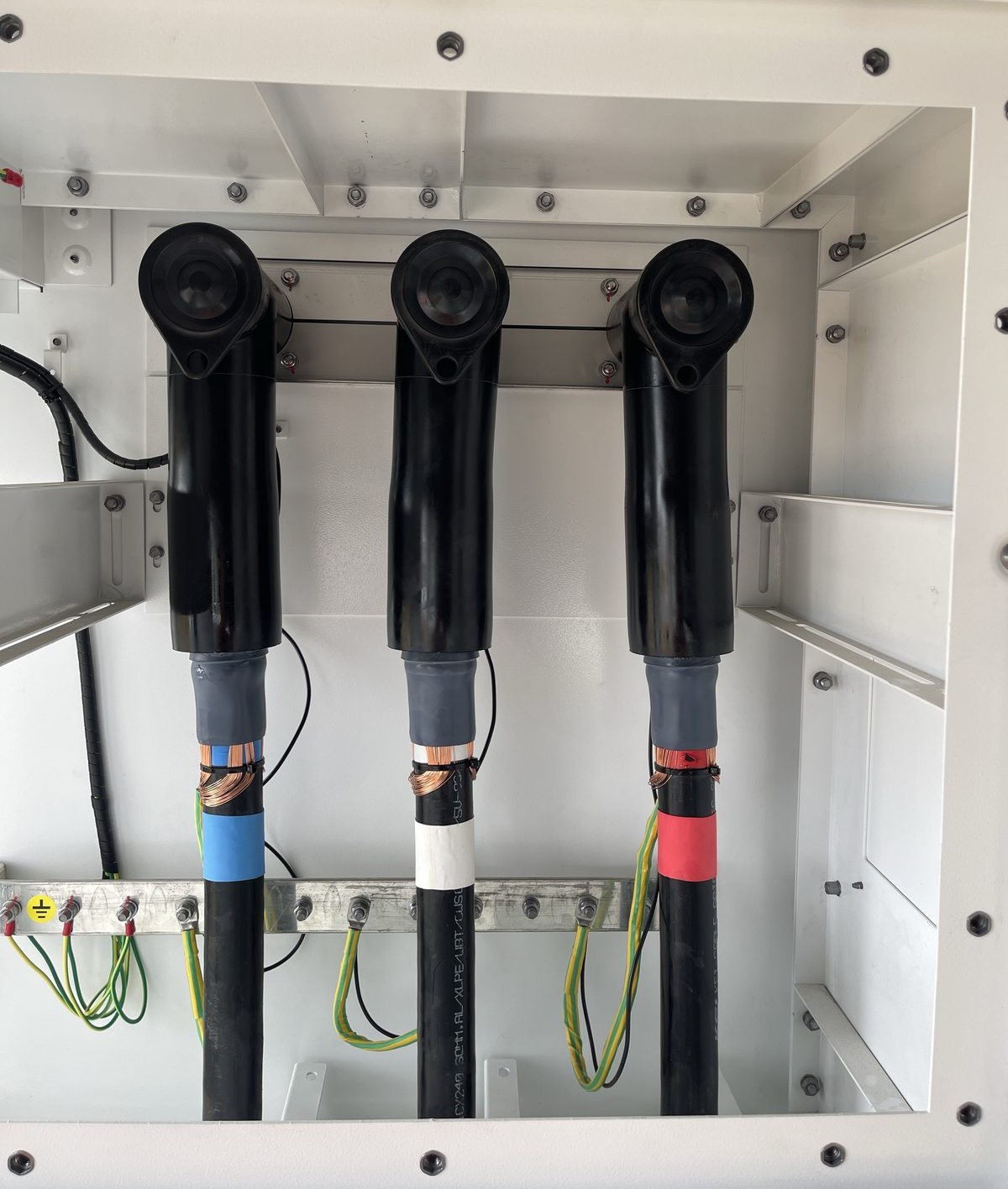 Three completed 33kV elbow terminations neatly dressed into an RMU cubicle with earthing in place — clean finished-work 