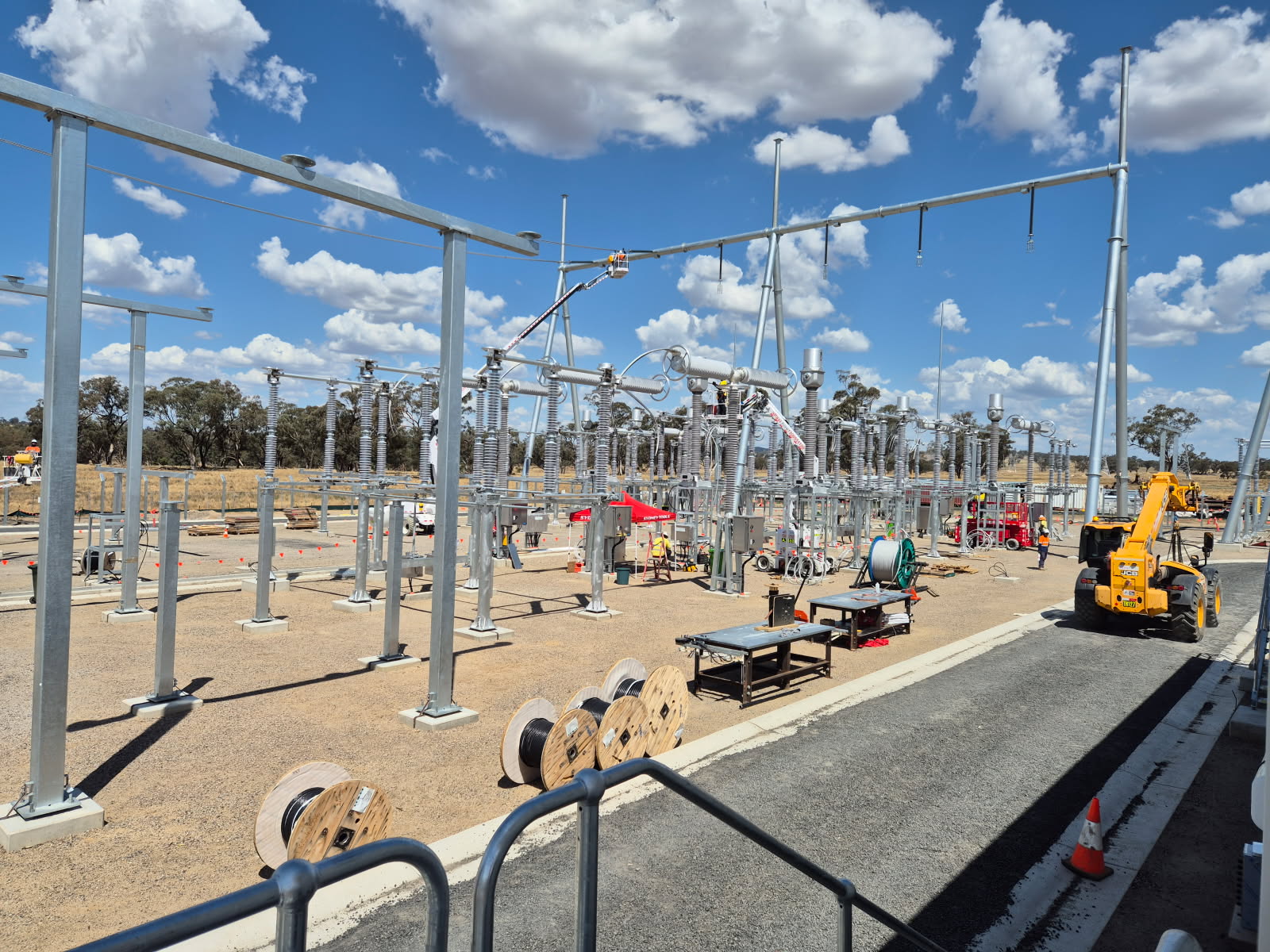 Wide view of the Uungula wind farm substation under construction — rows of high-voltage switchgear and insulator stacks under a blue sky, cable drums and crews on the gravel pad